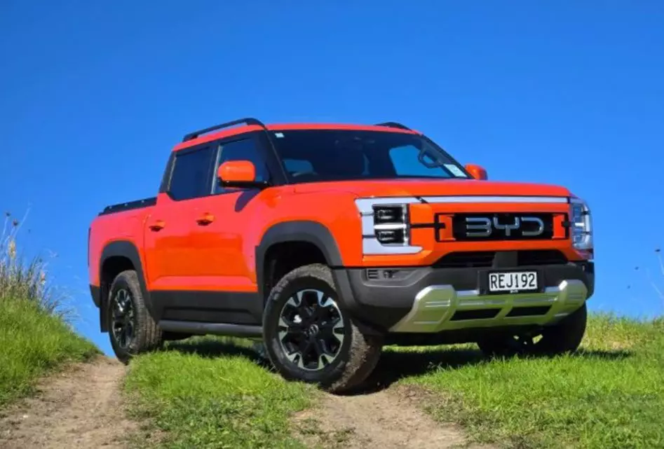 Orange BYD Shark 6 plug-in hybrid ute on grassy hillside