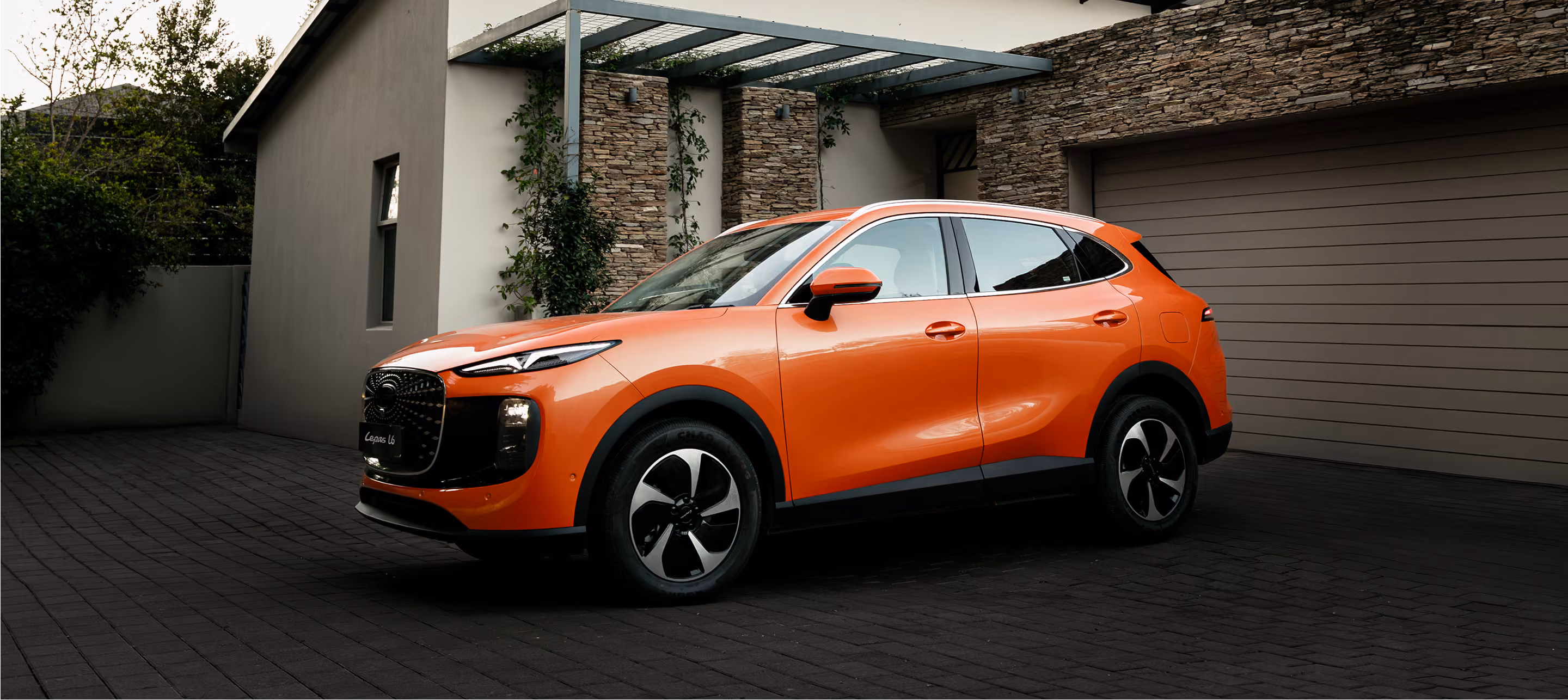 Orange Lepas L6 SUV in front of a modern home; South African-market ICE model shown.